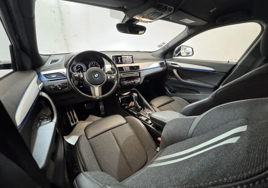Intérieur BMW X2 xDrive25e M Sport 2021 vu côté conducteur, sièges noirs et bandeau bleu sur tableau de bord.