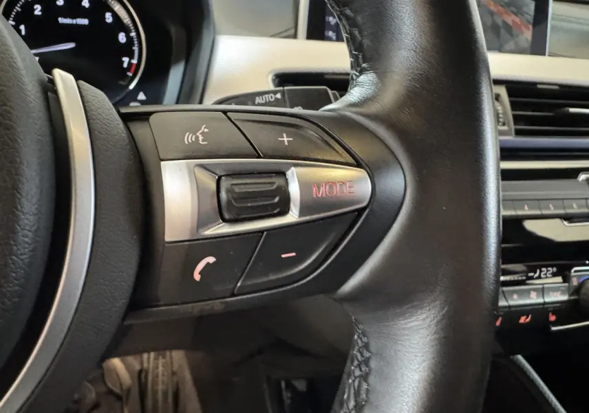 Gros plan sur les commandes multifonctions du volant cuir noir du BMW X2 xDrive25e M Sport 2021, intérieur moderne.