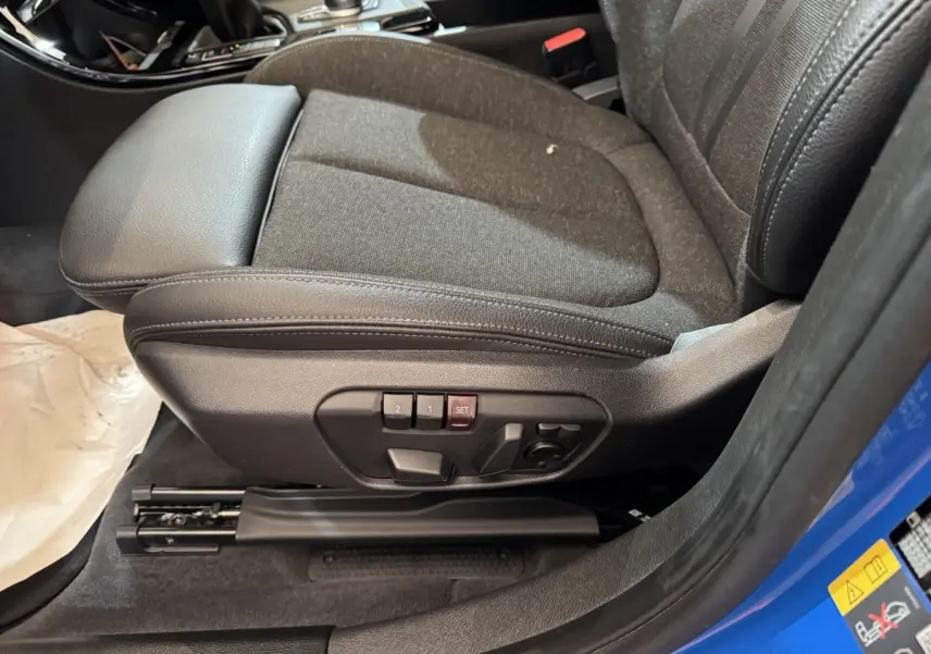 Gros plan sur le siège avant gauche noir avec réglages électriques, bordure de portière bleu visible d’une BMW X2 hybride.