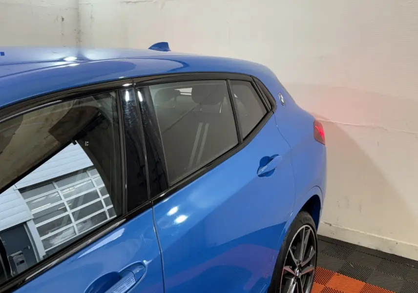 Vue 3/4 arrière côté gauche du BMW X2 xDrive25e M Sport bleu avec jantes sport et feux arrière allumés.