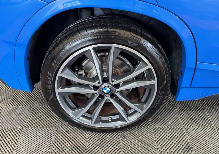 Gros plan sur la roue avant droite d’un BMW X2 bleu, avec jante alliage grise et logo BMW central.