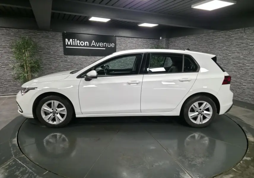 Vue de profil côté gauche d'une Volkswagen Golf VIII blanche, avec jantes alliage et poignées couleur carrosserie.