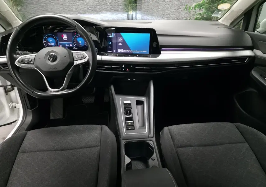Vue intérieure avant de la Volkswagen Golf VIII blanche, tableau de bord moderne avec écran tactile et volant multifonction.