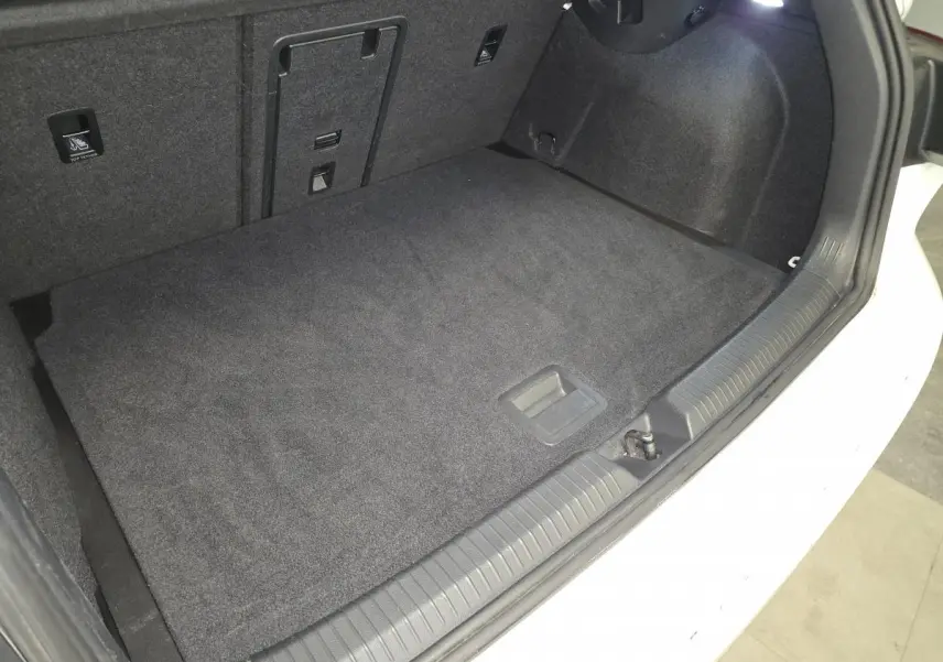 Coffre ouvert d’une Volkswagen Golf VIII blanche, montrant le tapis de sol et l’éclairage intérieur du coffre.