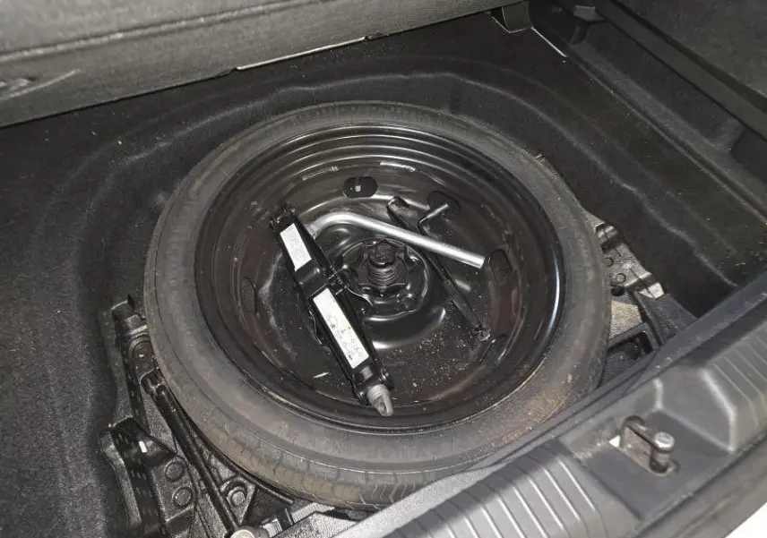 Gros plan sur la roue de secours noire et le cric dans le coffre d'une Volkswagen Golf VIII blanche.