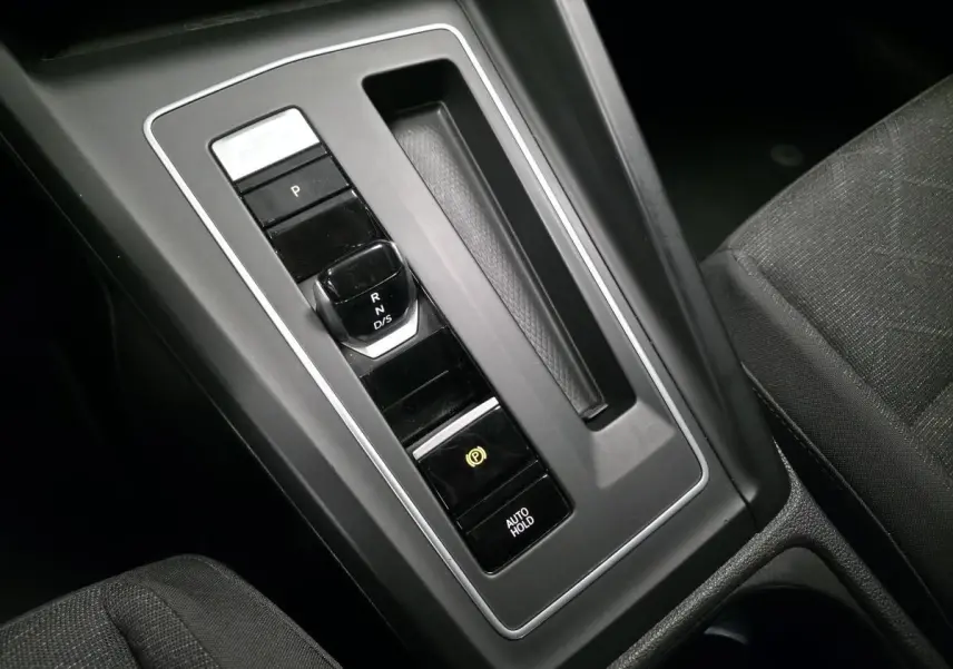 Gros plan sur la console centrale noire de la Volkswagen Golf VIII blanche, mettant en valeur le levier de vitesse automatique.