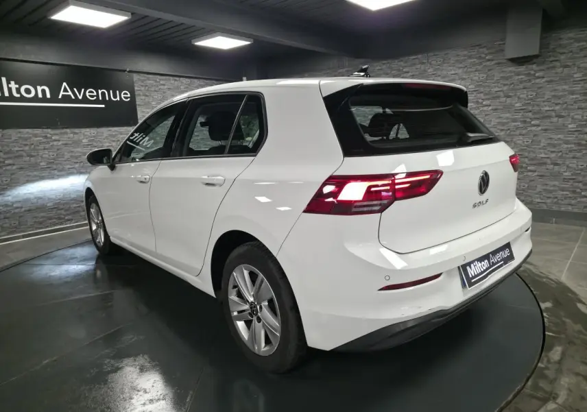 Volkswagen Golf VIII blanche vue 3/4 arrière droit en intérieur avec feux arrière allumés.