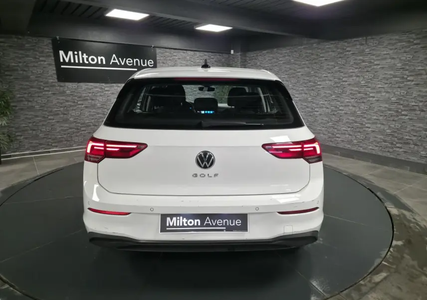 Vue arrière d'une Volkswagen Golf VIII blanche avec feux arrière LED allumés dans un showroom.