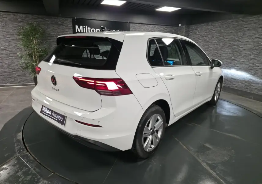 Volkswagen Golf VIII blanche vue 3/4 arrière droit en intérieur avec feux arrière LED allumés.