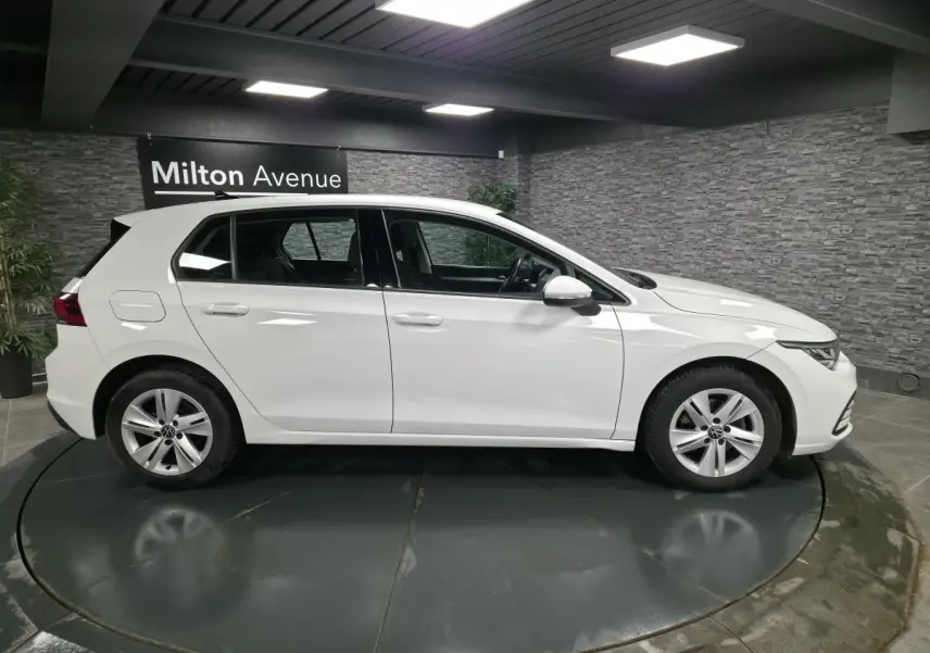 Profil côté gauche d'une Volkswagen Golf VIII blanche, en intérieur avec jantes alliage et éclairage LED au plafond.