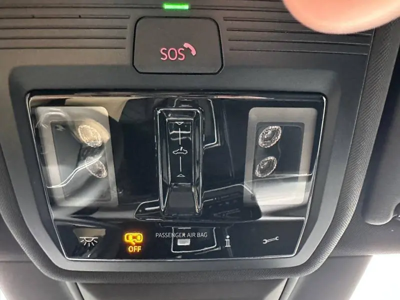 Vue en gros plan du panneau de commande intérieur noir avec bouton SOS rouge et indicateur airbag passager éteint sur Volkswagen Golf gris.