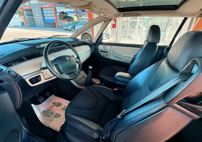 Intérieur de Renault Avantime gris, vue côté conducteur montrant sièges cuir noirs et tableau de bord clair avec toit panoramique.