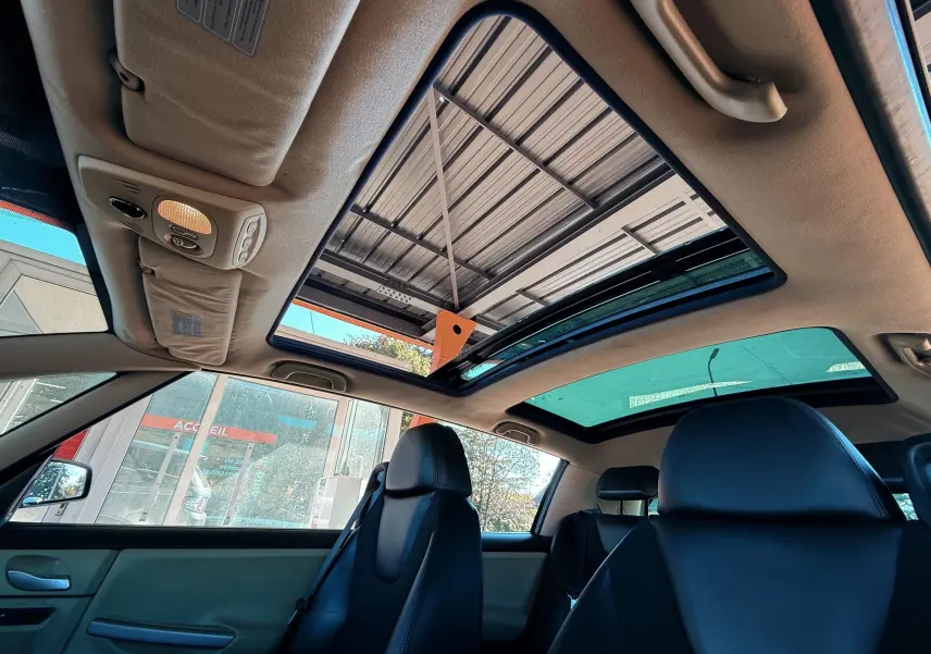 Vue intérieure du Renault Avantime gris montrant les sièges avant en cuir noir et le toit panoramique ouvert.