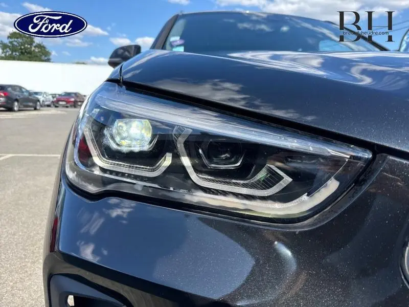 Gros plan sur le phare avant gauche d’un BMW X1 xDrive25eA 2021 en Saphirschwarz avec détails LED distinctifs.