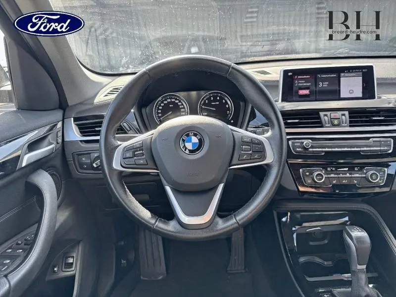 Intérieur du BMW X1 xDrive25e 2021 en Saphirschwarz, vue frontale sur le volant cuir multifonction et tableau de bord numérique.