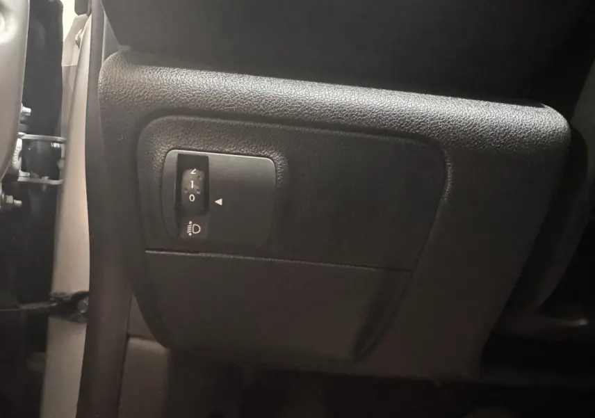 Gros plan sur le réglage de hauteur des phares côté gauche dans l’habitacle gris foncé de la Renault Mégane Business.