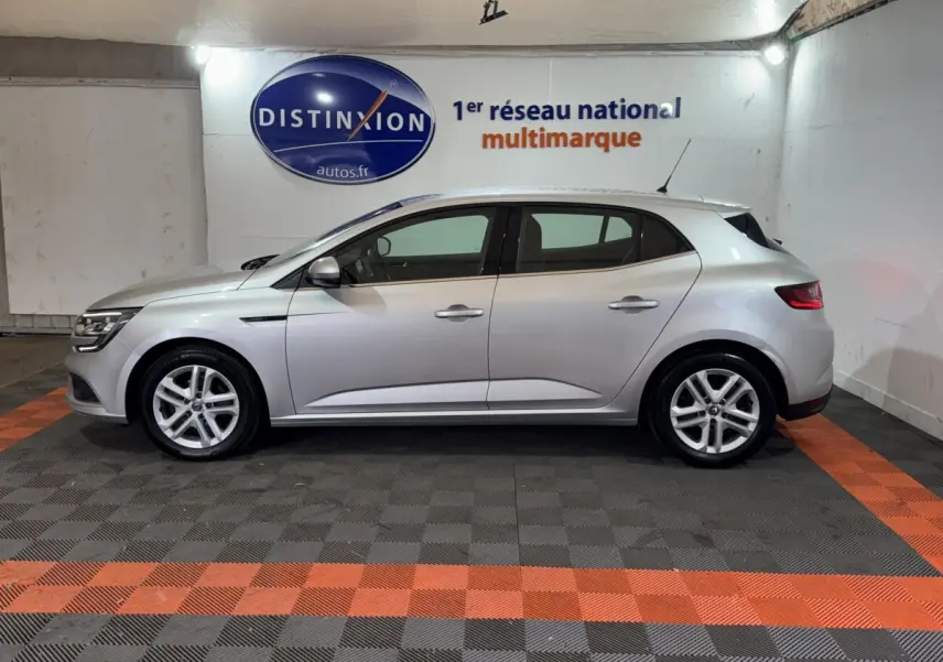 Profil droit d'une Renault Mégane Business gris clair, en intérieur sur sol à damiers gris et orange, avec logo Distinxion en arrière-plan.