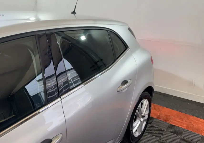 Vue côté droit arrière d'une Renault Mégane Business gris clair, avec jante alliage et vitres teintées.