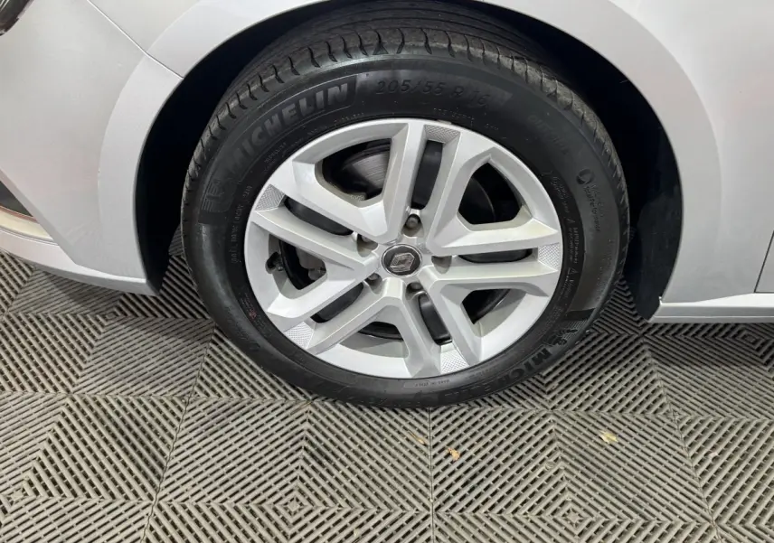 Vue rapprochée de la roue arrière droite d'une Renault Mégane Business gris clair sur sol texturé.