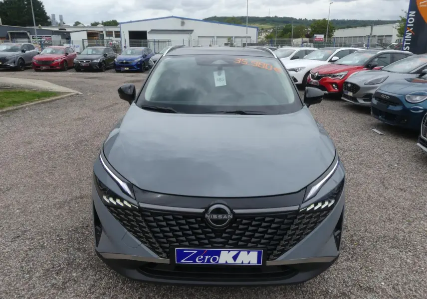 Vue avant d'un Nissan Qashqai gris métallisé avec calandre noire et feux LED distinctifs, stationné en extérieur.