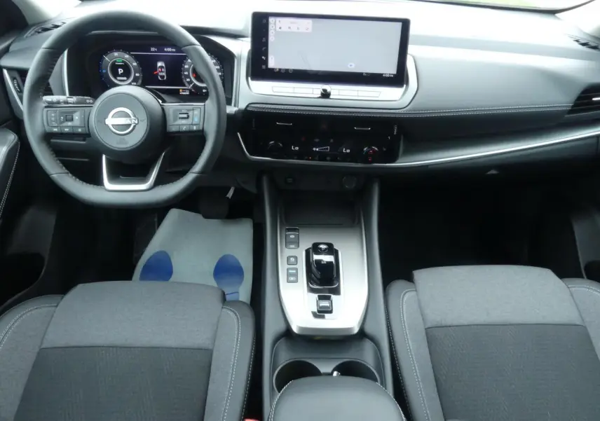 Vue intérieure avant du Nissan Qashqai 1.5 e-Power 2025, tableau de bord moderne avec écran tactile large et sellerie grise.