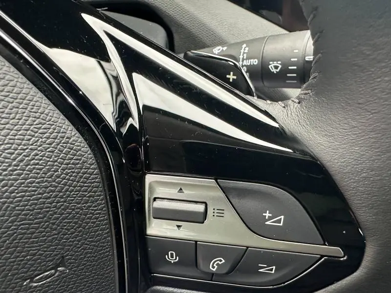 Gros plan sur les commandes au volant côté gauche de la Peugeot 308 2024 en Noir Perla Nera, avec boutons multifonctions et palettes.