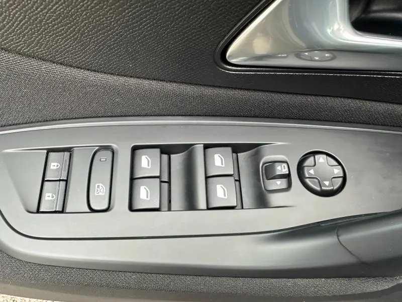 Gros plan sur les commandes des vitres et des rétroviseurs côté gauche de la porte intérieure d'une Peugeot 308 2024 noir Perla Nera.