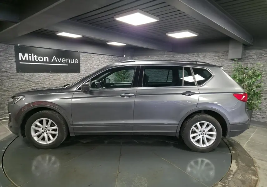 Vue de profil côté gauche d’un SEAT Tarraco gris, SUV 7 places avec jantes alliage 17 pouces dans un showroom.
