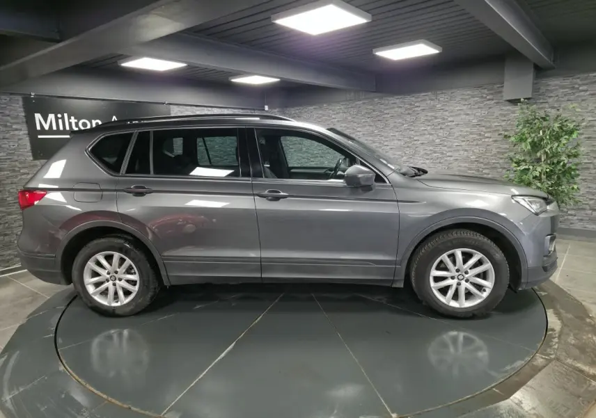 Vue de profil côté gauche d'un SEAT Tarraco gris, SUV 7 places, sur jantes alliage 17 pouces dans un showroom.