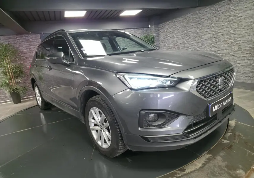 SEAT Tarraco gris en 3/4 avant droit, avec phares LED allumés et jantes alliage 17 pouces visibles.