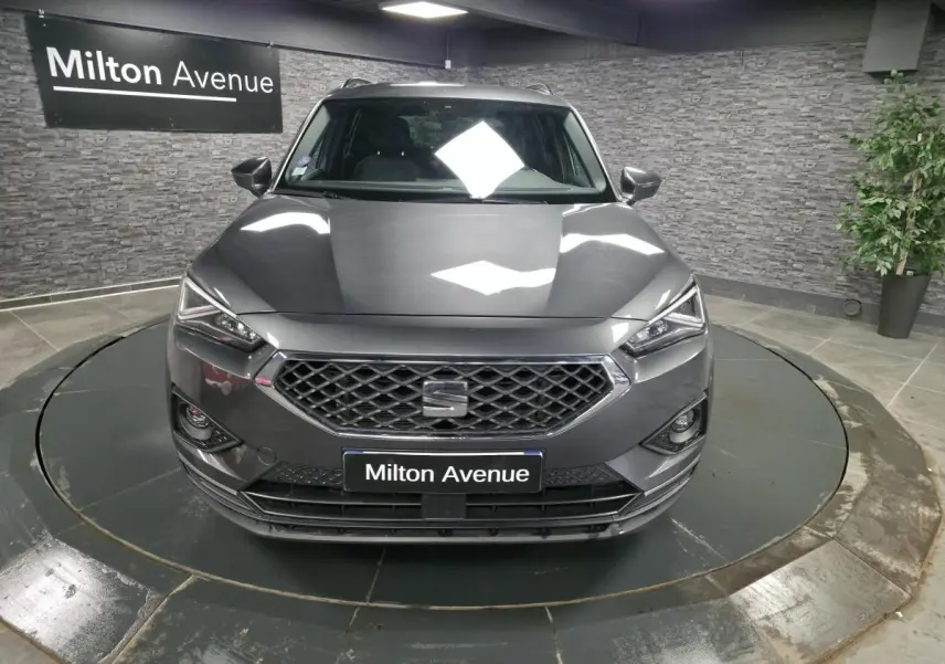 Vue avant d'un SEAT Tarraco gris Urano avec calandre hexagonale et phares Full LED dans un showroom.