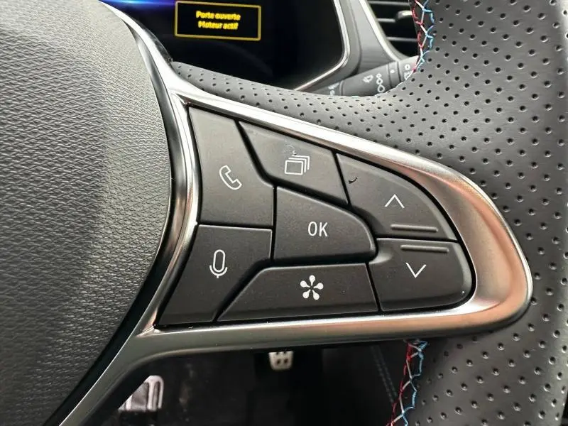 Gros plan sur les commandes au volant côté droit du Renault Captur 2026, avec surpiqûres tricolores et cuir perforé noir.