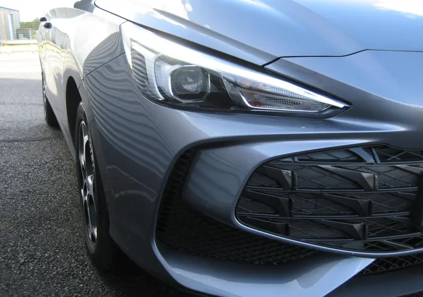 Gros plan sur l'avant droit gris du MG3 1.5 Hybrid 195CV Luxury, mettant en valeur le phare et la calandre ajourée.