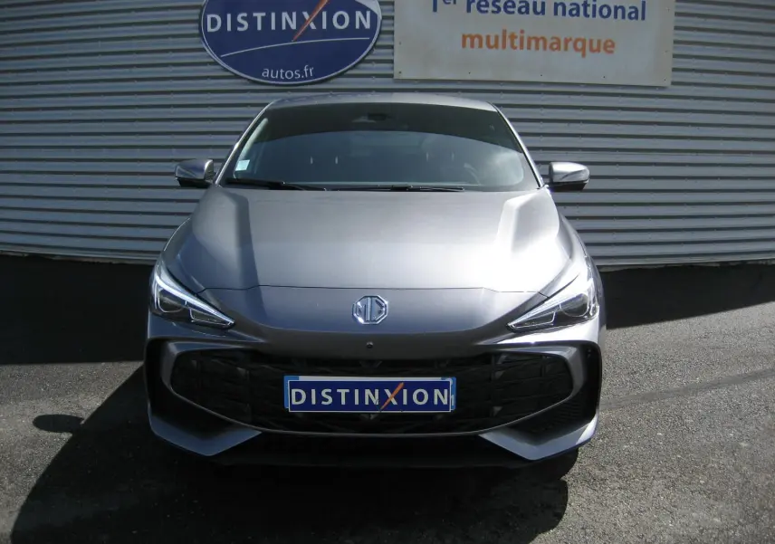 Vue de face d'une MG3 gris métallisé 2025 avec calandre noire et phares LED, devant un mur avec enseigne Distinxion.