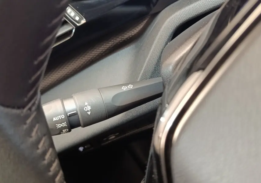 Gros plan sur la manette de clignotants et commandes d’éclairage côté gauche du volant cuir d’une Peugeot 308 verte.