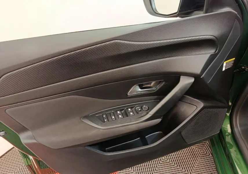 Vue intérieure côté gauche de la porte avant verte d'une Peugeot 308 avec commandes des vitres et haut-parleur intégré.