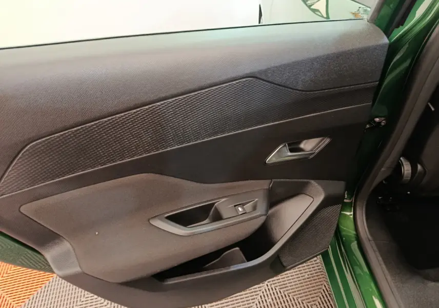 Vue intérieure sur la porte arrière gauche d'une Peugeot 308 2023 vert avec commandes de vitre et haut-parleur intégré.