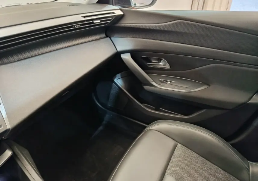 Vue intérieure côté passager de la Peugeot 308 2023, avec tableau de bord et porte en noir texturé.