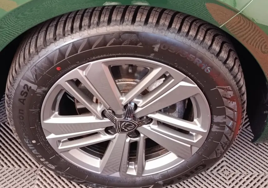 Gros plan sur la roue avant droite d'une Peugeot 308 vert 2023 avec jante alliage et logo Peugeot central.