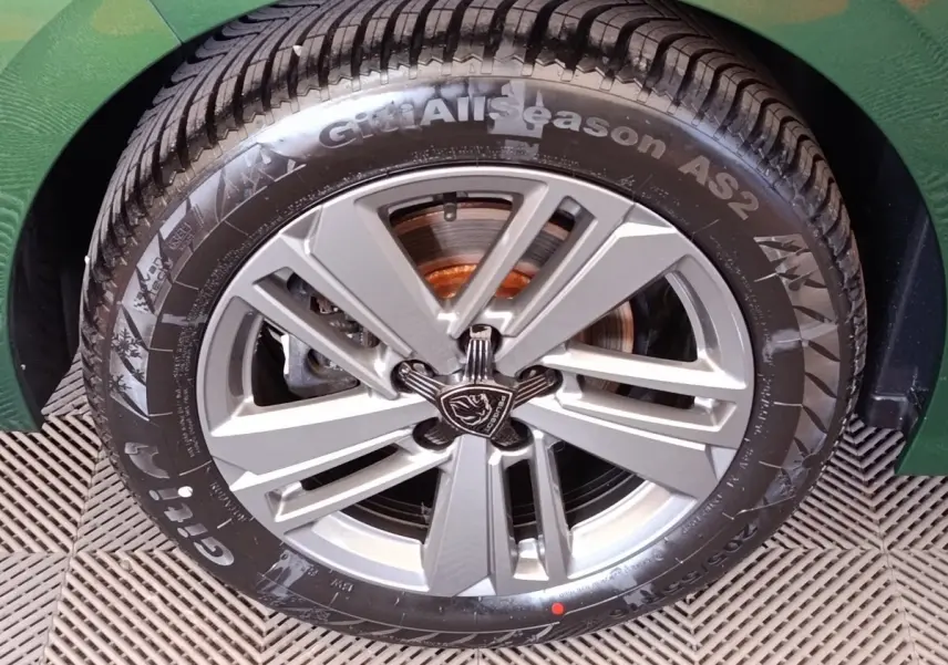 Gros plan sur la roue avant droite d'une Peugeot 308 vert 2023, mettant en valeur la jante alliage et le pneu toutes saisons.