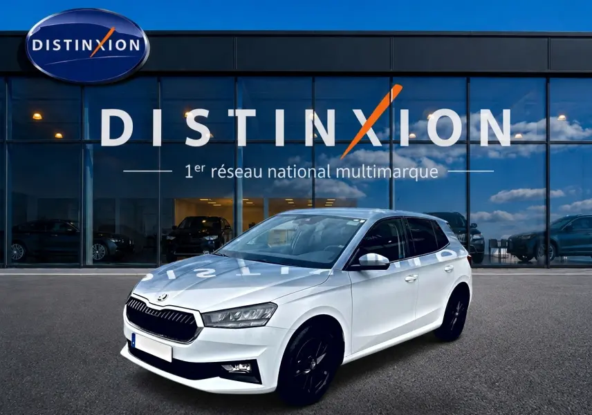 SKODA FABIA blanche vue en 3/4 avant droit, avec jantes noires et calandre distinctive devant un showroom Distinxion.