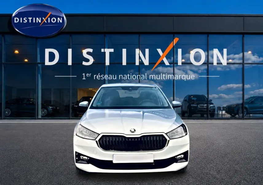 Vue avant d'une Skoda Fabia blanche 2025 avec calandre noire, garée devant une vitrine Distinxion.