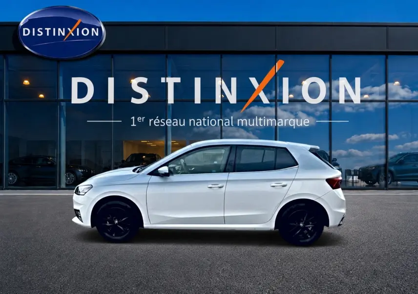 Vue latérale droite d'une Skoda Fabia blanche 2025 avec jantes noires, stationnée devant une vitrine Distinxion.