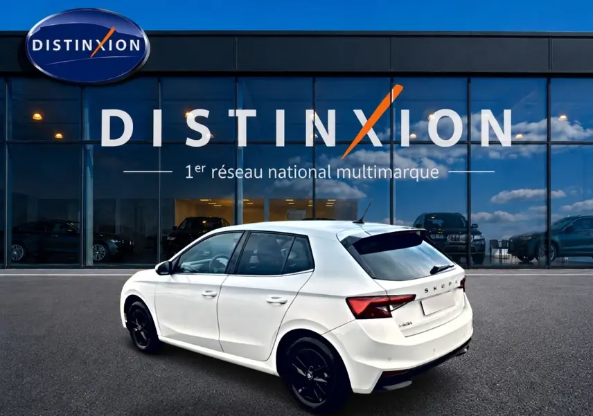 Vue 3/4 arrière droite d'une Skoda Fabia blanche 2025 avec jantes noires, stationnée devant une vitrine Distinxion.
