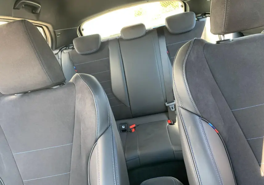 Intérieur de la BMW Série 1 118D M Sport 2025, vue arrière sur les sièges sport en Alcantara noir avec surpiqûres bleues.