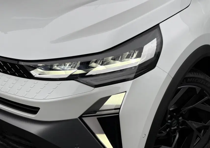 Gros plan sur l'avant droit du Renault Captur blanc nacré, mettant en valeur le phare LED et la jante aluminium noire.