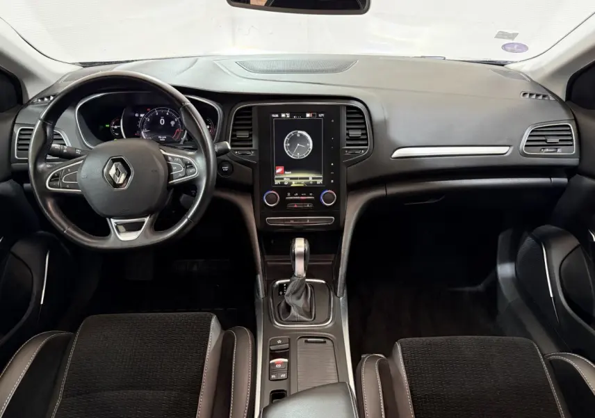 Vue intérieure avant de la Renault Mégane Intens 2019, tableau de bord noir avec écran tactile vertical et volant cuir multifonctions.