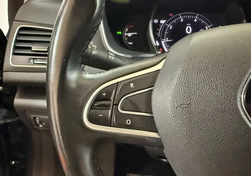 Gros plan sur le volant cuir noir de la Renault Mégane Intens, avec commandes intégrées et tableau de bord numérique en arrière-plan.