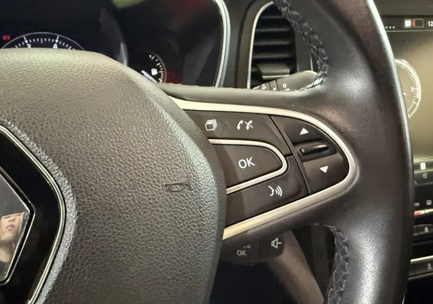 Gros plan sur le volant cuir multifonctions de la Renault Mégane Intens gris foncé avec commandes intégrées.