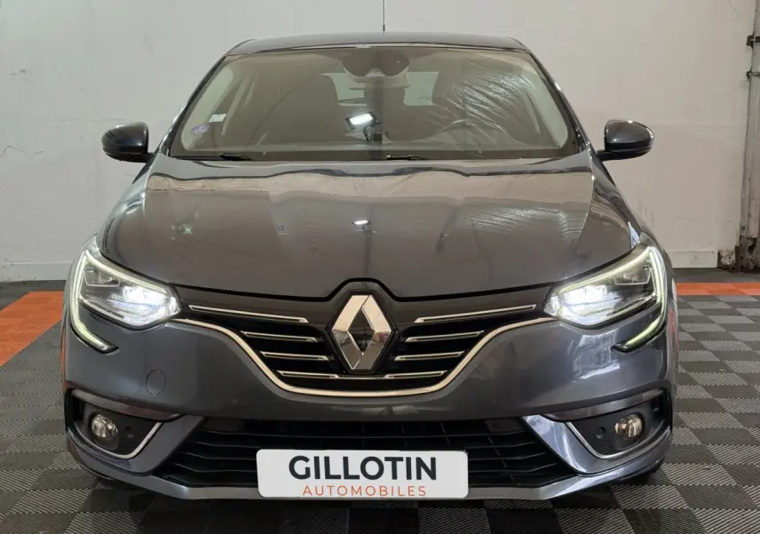 Vue frontale d'une Renault Mégane Intens gris foncé avec phares LED allumés et calandre chromée.